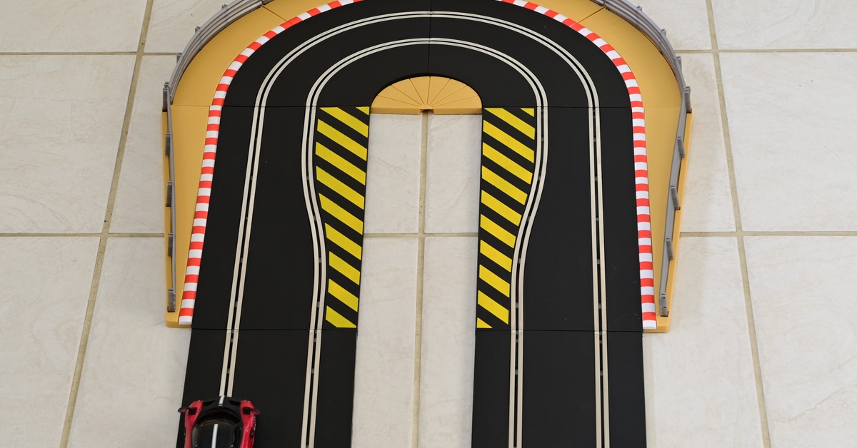 A hairpin turn of a slot car track on tiled ground. There is a red and black slot car driving along the track.
