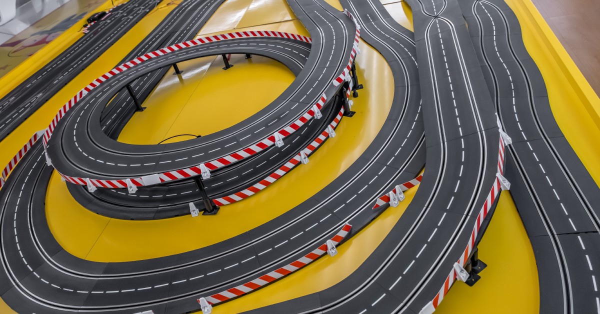 A large and winding toy race track set up on a yellow table. There are many curves and roundabouts in the track.
