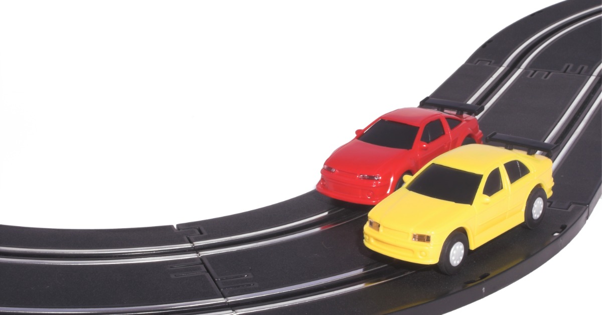 Two slot cars, one red and one yellow, racing against each other on a thin, black track with white stripes on it.