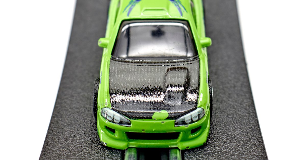 A close-up of a green slot car with a gray hood and a spoiler on the back. It is sitting on a racetrack.