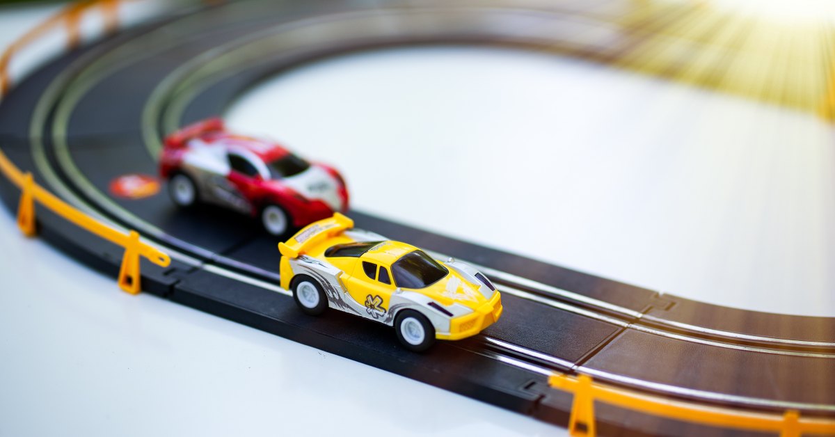On a small slot car track, a yellow and red car drive around in circles. the yellow is on the outside lane.
