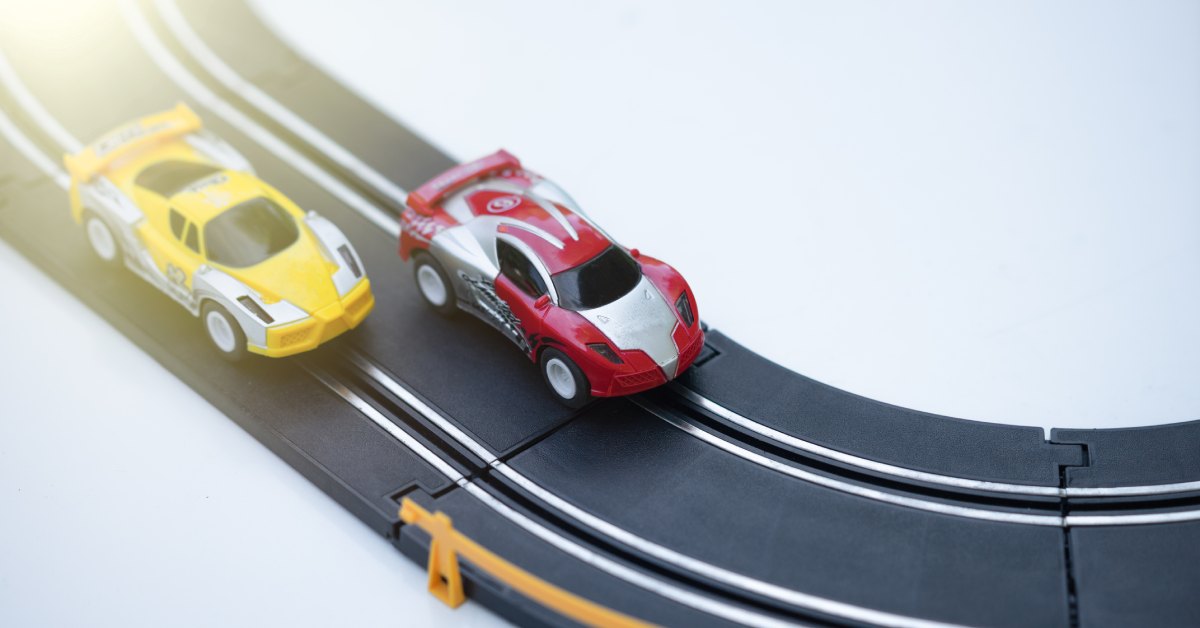 On a miniature slot car track, there are a red and yellow slot car driving. the red car is on the inside track.
