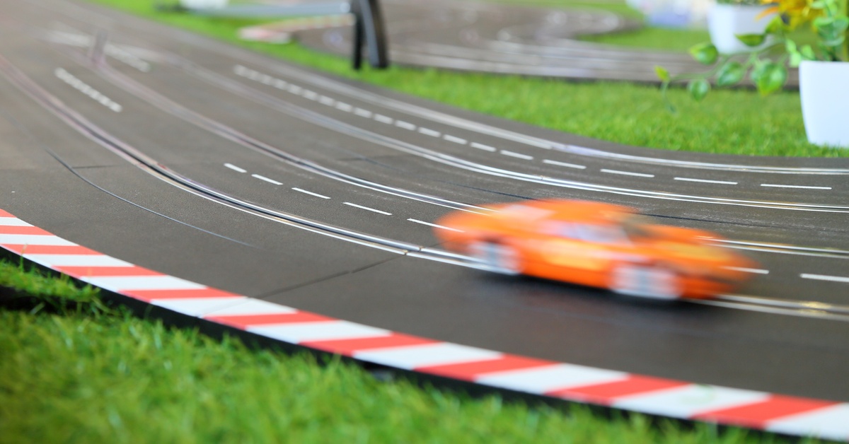 How To Succeed in Slot Car Racing Competitions A close up of a slot car track with multiple decorations and an orange slot car speeding by. The car is blurry as it drives by.