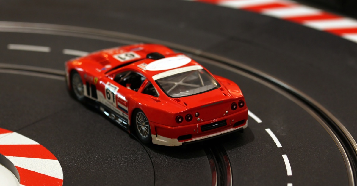 A close up a red slot car driving around a curve in the slot car track. The car is red with white spots and the number