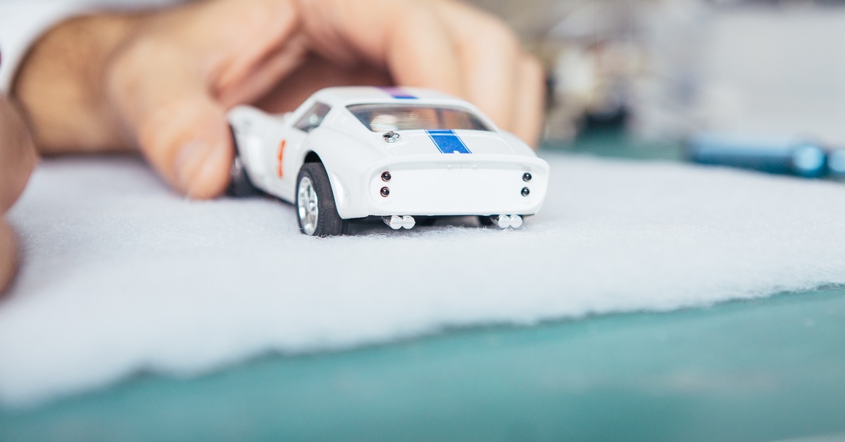 A hand holding a small slot car that has been painted white with a blue racing stripe. The car is on top of a white towel.
