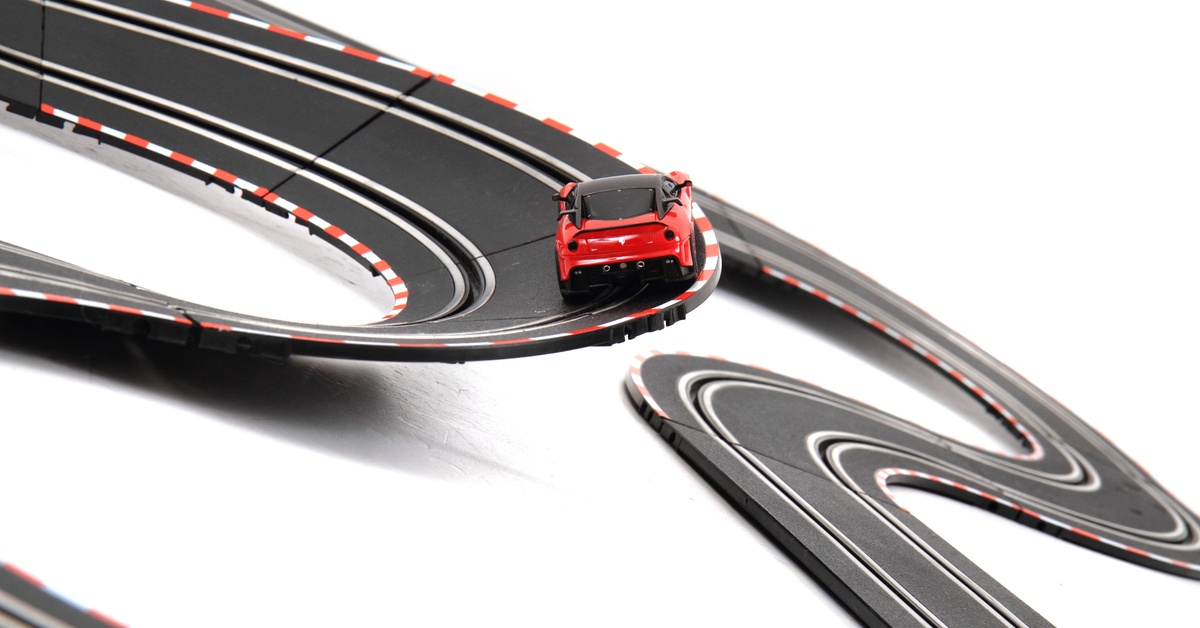 A stretch of slot car racing track making a sharp turn. There is a single, red slot car on the track making the turn.