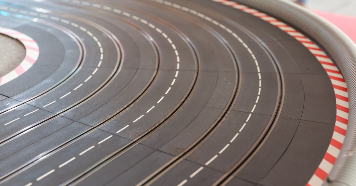 A close-up of a slot car racing track. The exterior has red and white stripes, and there's a plastic barrier.