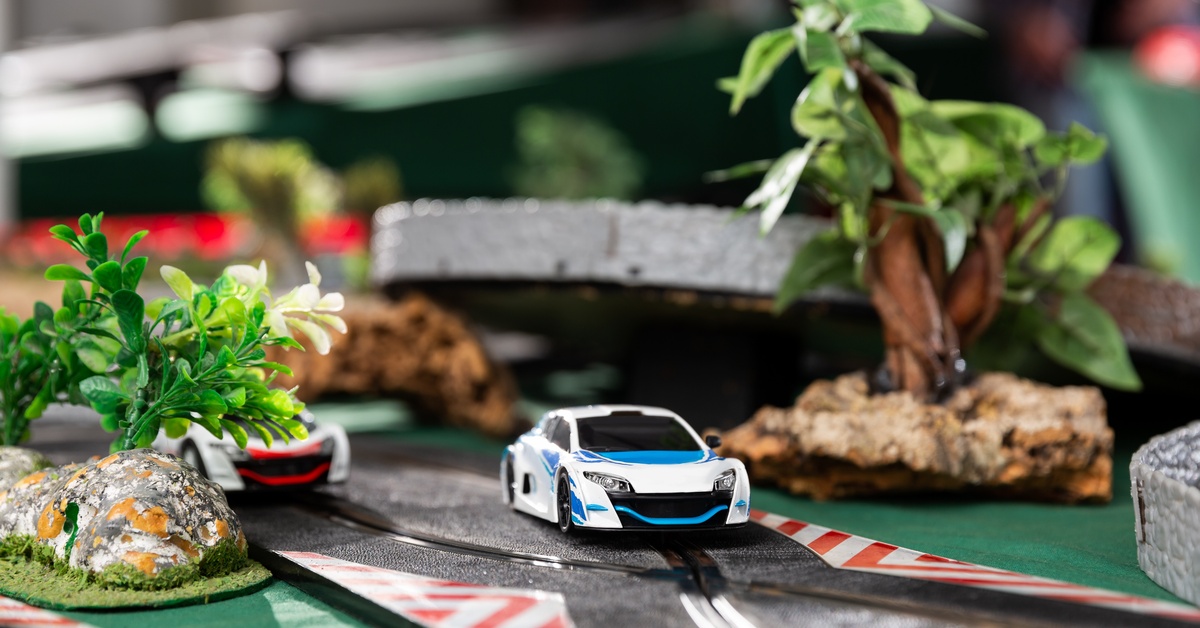 A slot car track with two different colored cars driving through various decorations like trees and rocks.